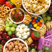 snack food such as popcorn, gummy bears, marshmallows, and grapes arranged in cups sitting close together.