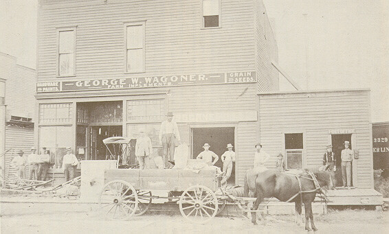 A group of men, two in a cart, as well as a horse stand in front of a building labelled "George W. Wagoner Farm Implements."