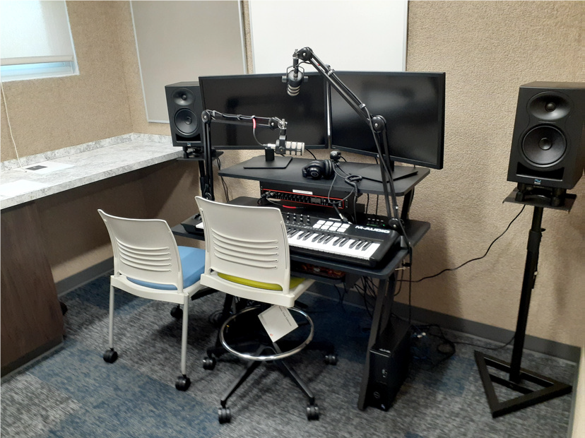 Two chairs sit before a keyboard and dual monitor setup, with a microphone arm swung before them.