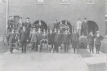 Two rows of men stand in front of a building for the photo.