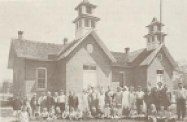 A group stands outside of a schoolhouse.